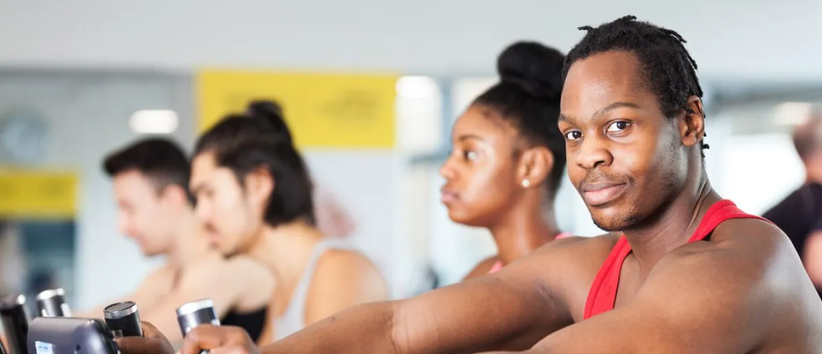 Four people working out in the LSBU gym, with one guy in a red vest looking at the camera.